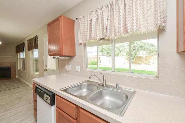 kitchen with dishwasher, sink, a tile fireplace, and light wood-type flooring