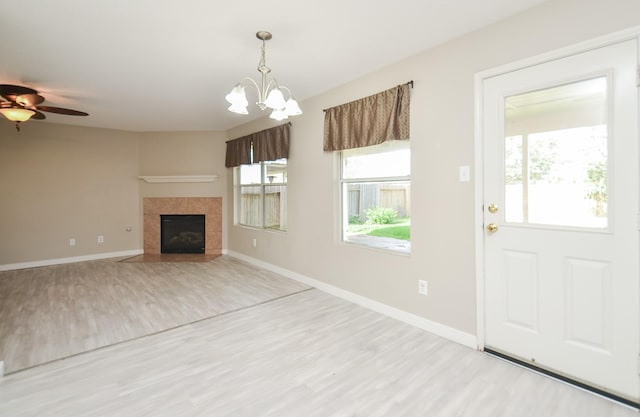 unfurnished living room with a tiled fireplace, ceiling fan with notable chandelier, and light wood-type flooring