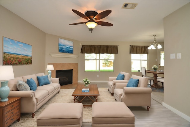 living room with a fireplace, ceiling fan with notable chandelier, and light wood-type flooring