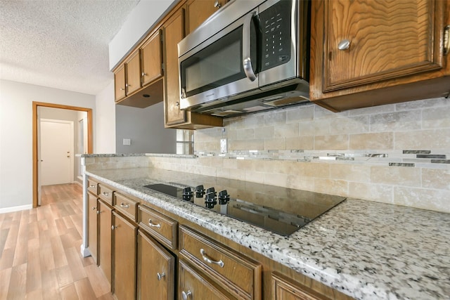 kitchen with tasteful backsplash, black electric stovetop, light hardwood / wood-style flooring, light stone countertops, and a textured ceiling