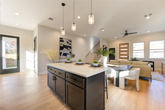 kitchen featuring ceiling fan, a center island, a breakfast bar, hanging light fixtures, and light wood-type flooring