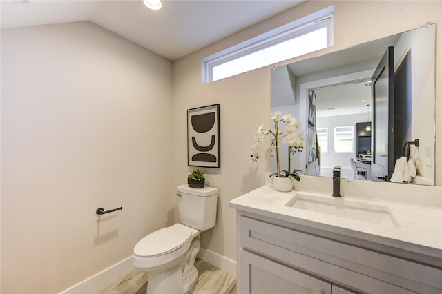 bathroom with toilet, a healthy amount of sunlight, vaulted ceiling, and vanity