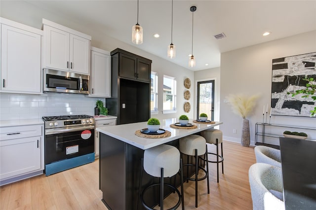 kitchen featuring pendant lighting, white cabinets, appliances with stainless steel finishes, a kitchen island, and decorative backsplash