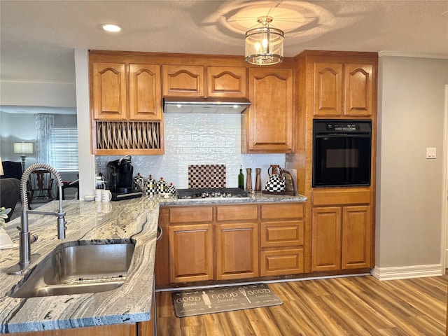 kitchen with sink, backsplash, light stone counters, oven, and light wood-type flooring