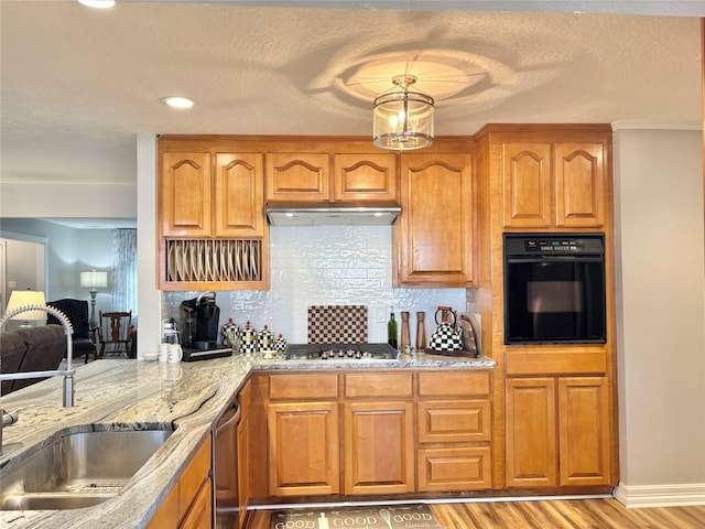 kitchen with appliances with stainless steel finishes, sink, light stone countertops, a textured ceiling, and light hardwood / wood-style flooring