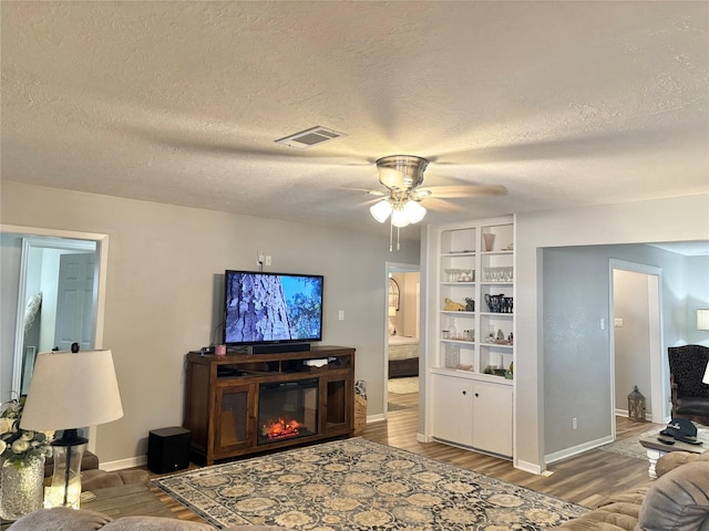 living room featuring hardwood / wood-style flooring, ceiling fan, built in features, and a textured ceiling