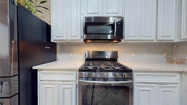 kitchen with light stone counters, backsplash, white cabinets, and appliances with stainless steel finishes