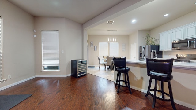 kitchen with sink, appliances with stainless steel finishes, a kitchen breakfast bar, white cabinets, and dark hardwood / wood-style flooring