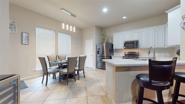 kitchen featuring appliances with stainless steel finishes, white cabinetry, light stone counters, a kitchen bar, and decorative light fixtures