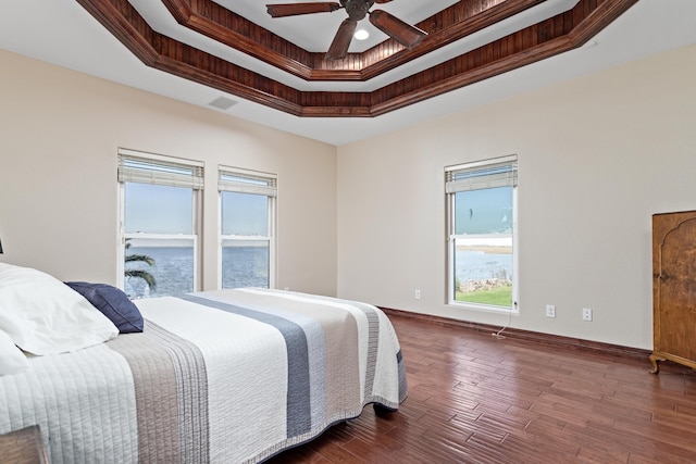 bedroom with ceiling fan, dark hardwood / wood-style floors, a raised ceiling, crown molding, and a water view