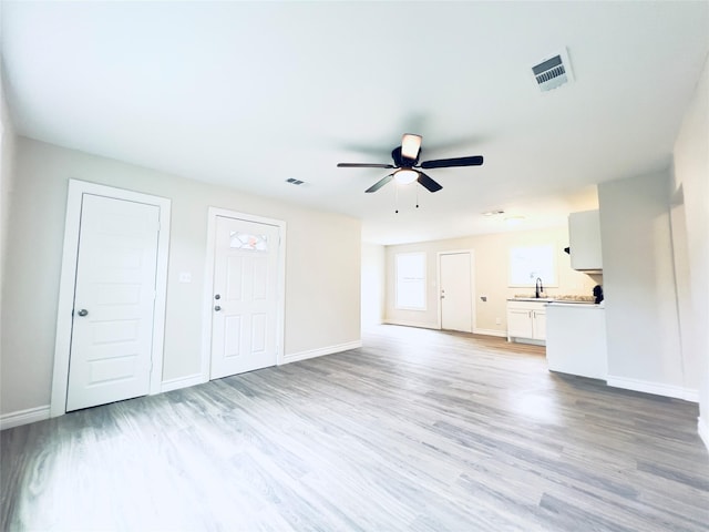 unfurnished living room with ceiling fan, sink, and light wood-type flooring