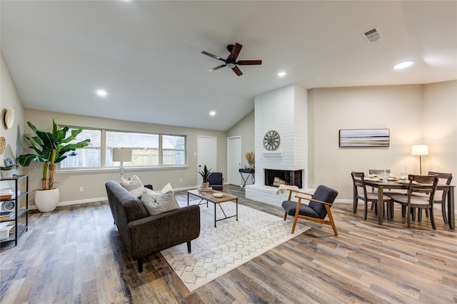 living room featuring ceiling fan, lofted ceiling, a fireplace, and wood-type flooring