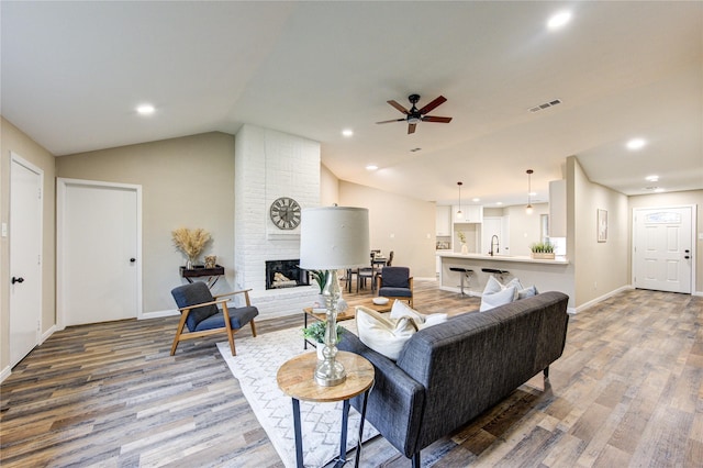 living room with ceiling fan, lofted ceiling, a fireplace, and wood-type flooring