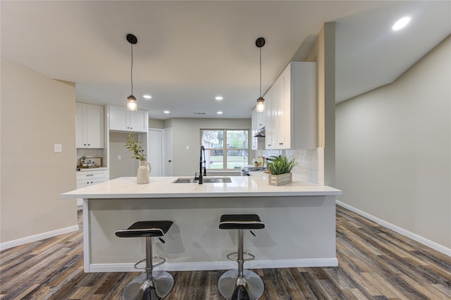 kitchen featuring white cabinets, dark wood-type flooring, decorative backsplash, sink, and a kitchen breakfast bar