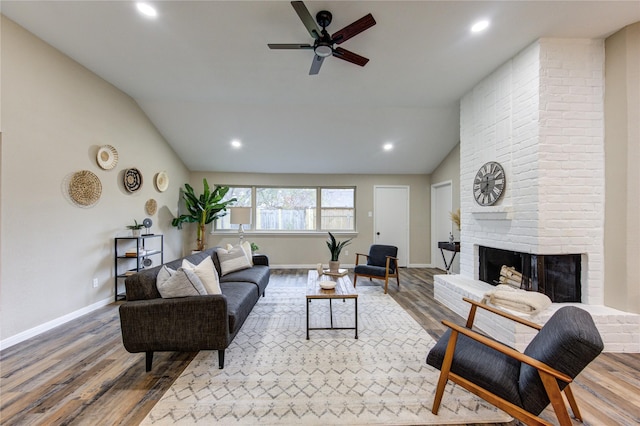 living room with hardwood / wood-style flooring, vaulted ceiling, ceiling fan, and a fireplace