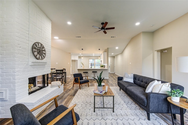 living room featuring a brick fireplace, light hardwood / wood-style floors, and ceiling fan