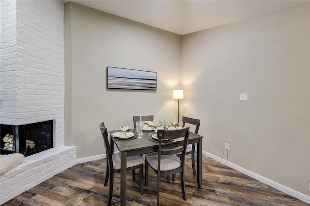 dining room with a brick fireplace and dark hardwood / wood-style floors