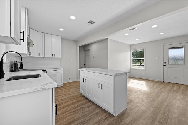 kitchen with a kitchen island, white cabinetry, light stone counters, and sink