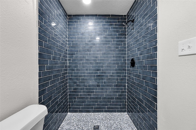 bathroom with a textured ceiling, toilet, and a tile shower