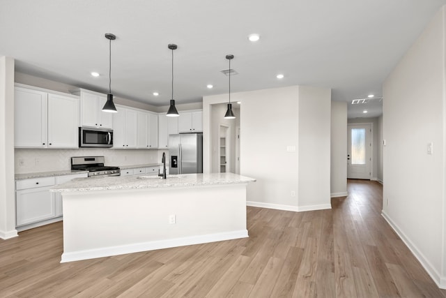 kitchen featuring stainless steel appliances, white cabinets, hanging light fixtures, and a kitchen island with sink