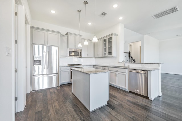 kitchen featuring stainless steel appliances, decorative light fixtures, dark wood-type flooring, a kitchen island, and light stone counters