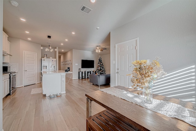 kitchen featuring pendant lighting, white cabinets, an island with sink, ceiling fan, and stainless steel range with gas stovetop