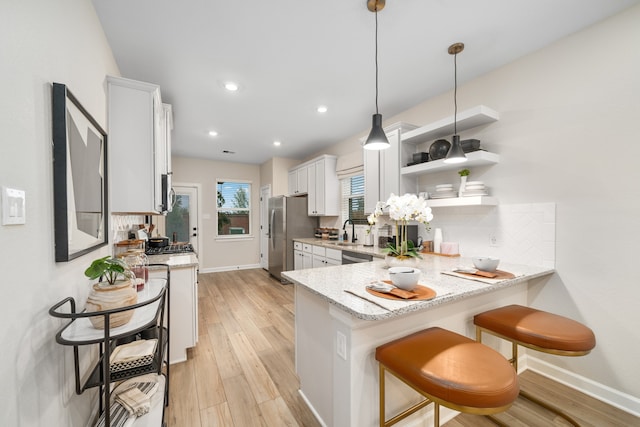 kitchen featuring decorative light fixtures, kitchen peninsula, white cabinetry, appliances with stainless steel finishes, and light stone countertops