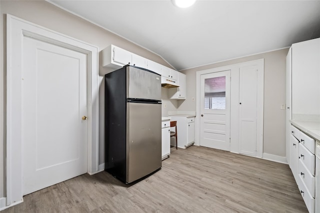 kitchen with lofted ceiling, white cabinets, stainless steel refrigerator, and light hardwood / wood-style floors