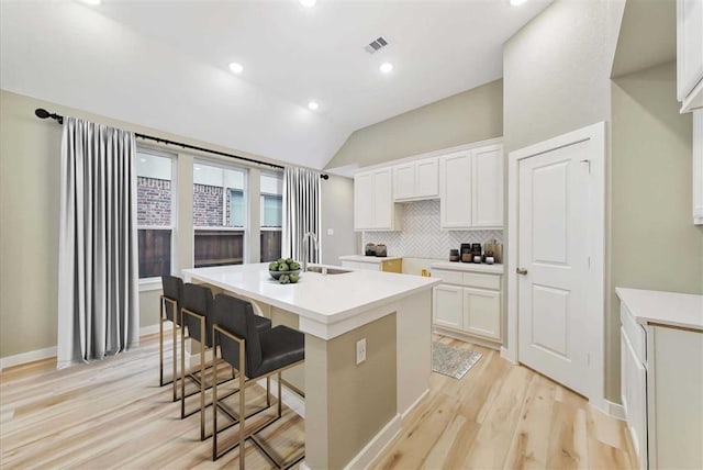 kitchen featuring lofted ceiling, white cabinets, sink, and a center island with sink