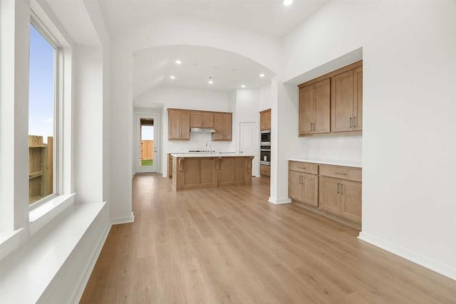 kitchen with sink, light wood-type flooring, a kitchen island with sink, and built in microwave