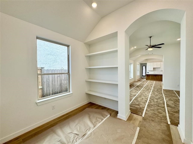 empty room with hardwood / wood-style flooring, ceiling fan, built in features, and lofted ceiling