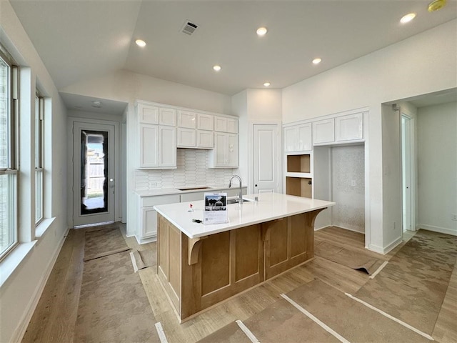 kitchen with an island with sink, backsplash, white cabinetry, and light wood-type flooring