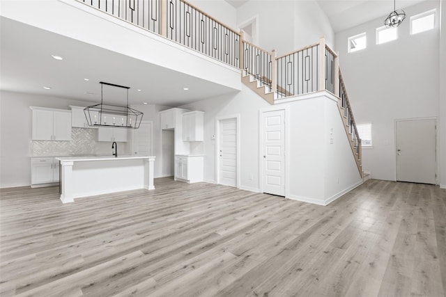 unfurnished living room featuring light wood-type flooring, a towering ceiling, and sink