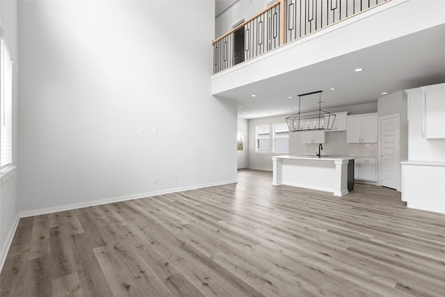 unfurnished living room featuring light hardwood / wood-style floors, sink, and a high ceiling