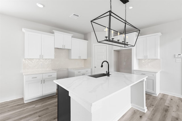 kitchen with sink, white cabinetry, and a kitchen island with sink