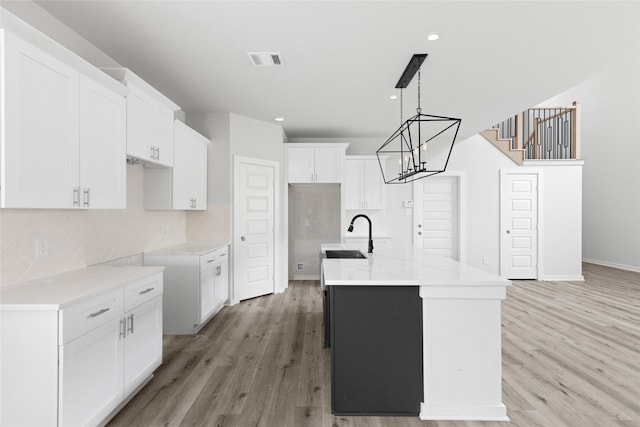 kitchen featuring white cabinetry, light hardwood / wood-style floors, a center island with sink, hanging light fixtures, and sink