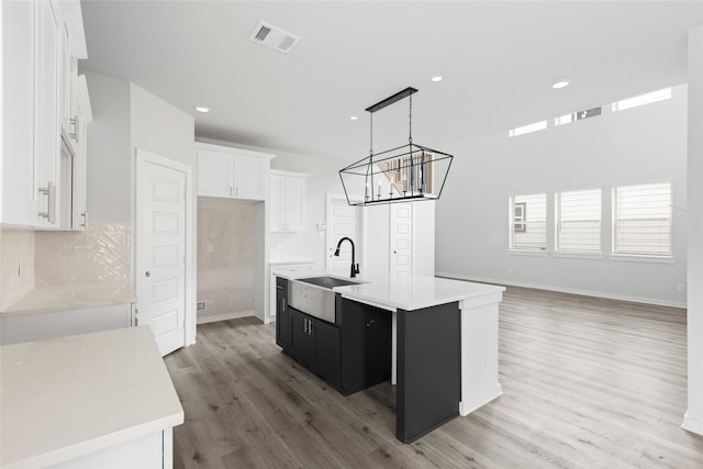 kitchen with white cabinetry, a center island with sink, decorative backsplash, pendant lighting, and sink