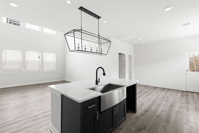 kitchen featuring a healthy amount of sunlight, sink, hanging light fixtures, a kitchen island with sink, and light hardwood / wood-style flooring