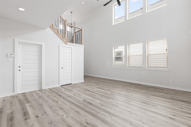 unfurnished living room with light wood-type flooring, a towering ceiling, a wealth of natural light, and a chandelier