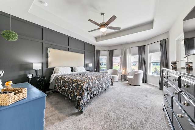 bedroom with light carpet, ceiling fan, and a tray ceiling