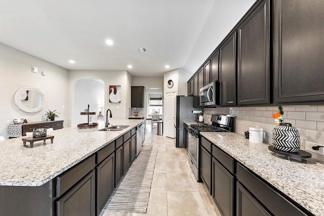 kitchen featuring appliances with stainless steel finishes, tasteful backsplash, sink, light stone counters, and a center island with sink