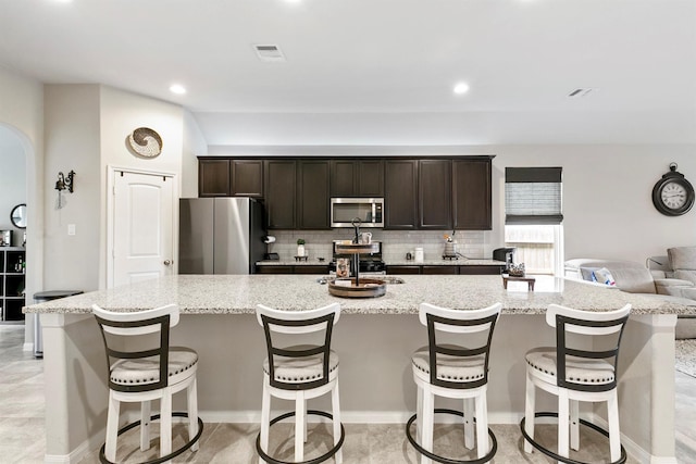 kitchen featuring dark brown cabinets, a breakfast bar area, stainless steel appliances, and a large island with sink