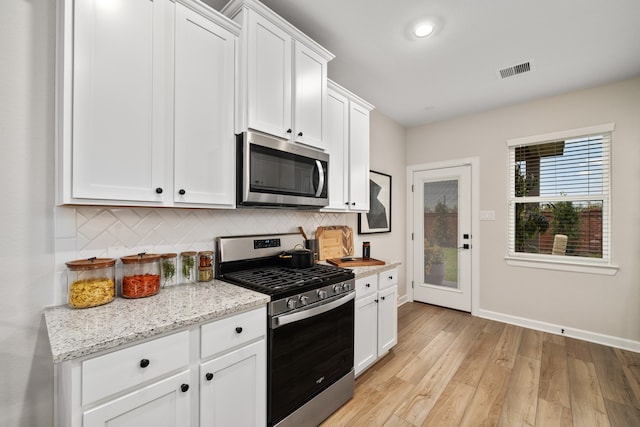 kitchen with stainless steel appliances, tasteful backsplash, white cabinets, light stone countertops, and light hardwood / wood-style flooring