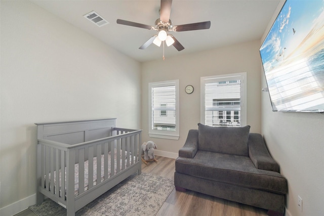 bedroom with ceiling fan, light hardwood / wood-style flooring, and a crib