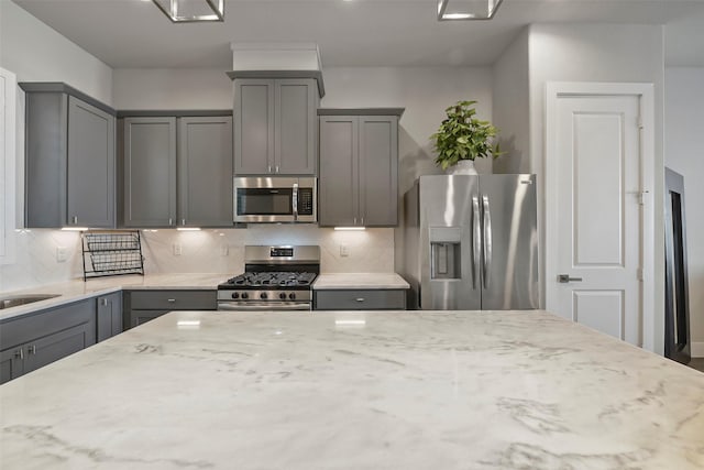 kitchen with appliances with stainless steel finishes, gray cabinetry, and light stone countertops