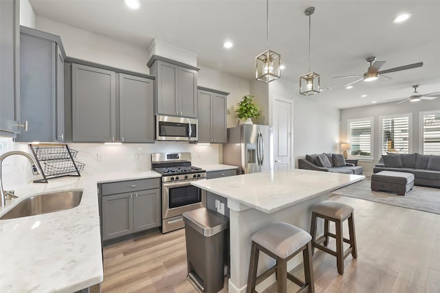 kitchen with gray cabinets, stainless steel appliances, light stone counters, a breakfast bar, and sink