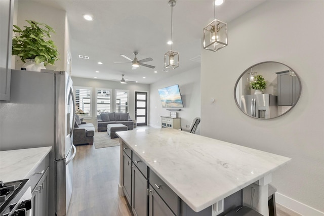 kitchen featuring gray cabinets, appliances with stainless steel finishes, pendant lighting, light stone counters, and a center island