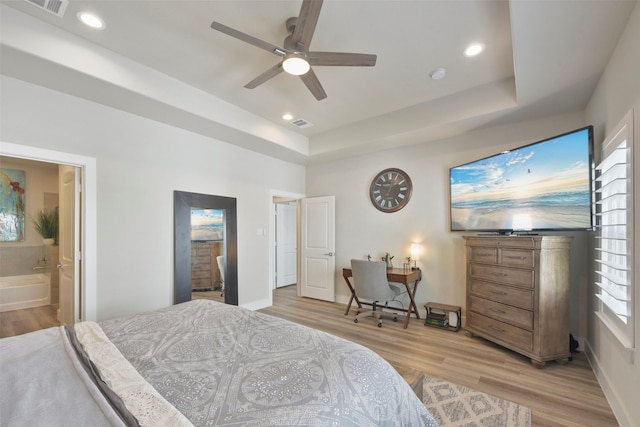 bedroom featuring light hardwood / wood-style flooring, ceiling fan, connected bathroom, and a raised ceiling