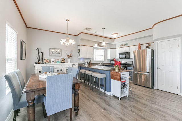 dining room featuring light wood-type flooring, a notable chandelier, sink, and ornamental molding