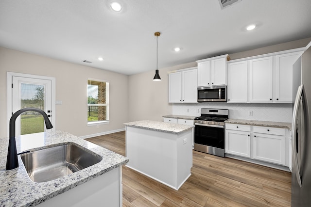 kitchen with decorative light fixtures, a kitchen island, sink, white cabinetry, and stainless steel appliances